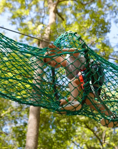 Un garçon en train de faire un parcours aventure dans un filet dans les arbres